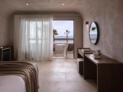 Modern hotelkamer met balkon, zeezicht en minimalistische meubels in warme tinten.