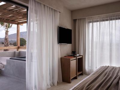 Hotelkamer met gordijnen, tv, nachtkastje en uitzicht op een terras met zitgedeelte.