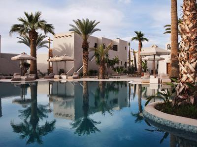 Modern hotelzwembad met palmbomen en parasols onder een blauwe lucht.