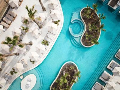 Modern hotelzwembad met parasols, ligstoelen en beplante eilanden in het water.