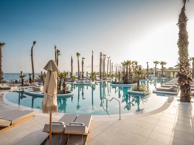 Nowoczesny hotelowy basen z palmami i leżakami przy morzu o zachodzie słońca.