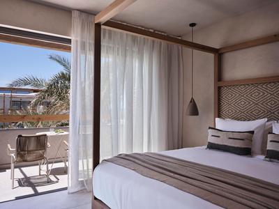 Lichte hotelkamer met groot bed, balkon en uitzicht op palmbomen.