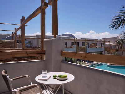 Balkon met tafel, stoel, glas water en uitzicht op zwembad en meerdere gebouwen.