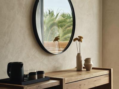 Table en bois moderne avec miroir rond et vases devant un mur couleur sable
