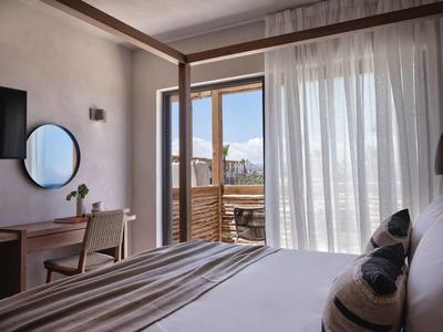 Chambre d'hôtel lumineuse avec lit double, bureau et porte donnant sur un balcon avec vue sur la montagne.