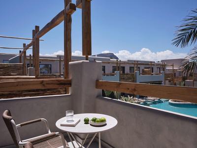 Vue de la terrasse avec petite table ronde, chaise, verre d'eau et piscine en arrière-plan