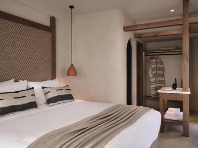 Chambre d'hôtel moderne avec grand lit, tête de lit décorative, mobilier en bois et éclairage chaleureux.