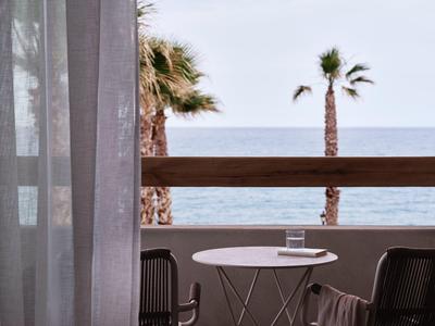Balcon avec petite table ronde, deux chaises, vue sur des palmiers et la mer en arrière-plan.