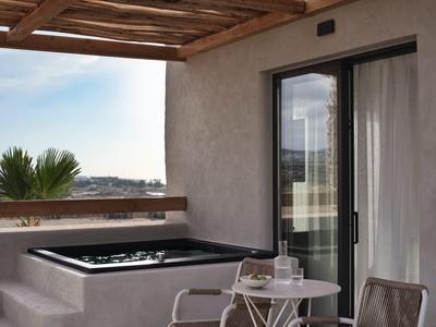 Balcon avec jacuzzi, petite table et chaise près de la porte vitrée, vue sur des palmiers et le paysage.