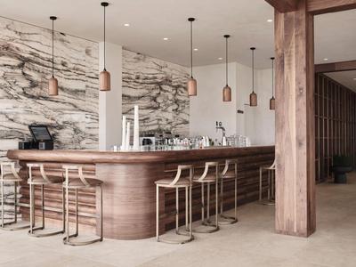 Moderne hotelbar met marmeren muur, houten balie en lichtgekleurde barkrukken.