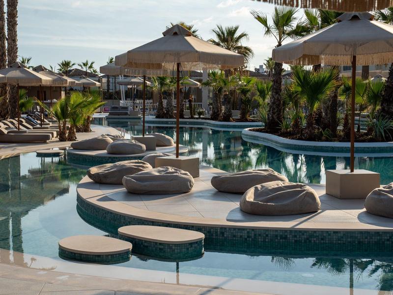 Piscine d'hôtel moderne avec chaises longues et parasols, entourée de palmiers.
