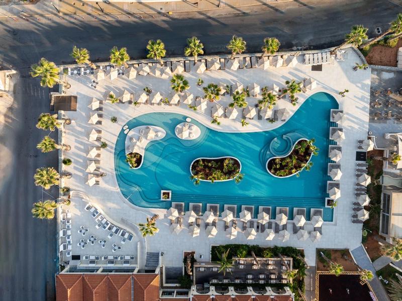 Vue drone d'un hôtel avec grande piscine, transats et palmiers sur la terrasse.
