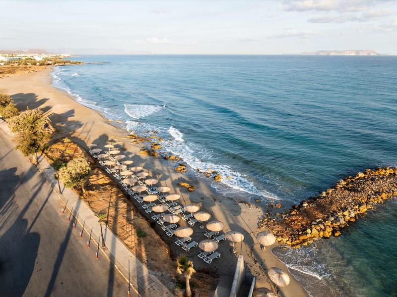 Longue plage de sable avec parasols et chaises longues près de la mer calme et des rochers.