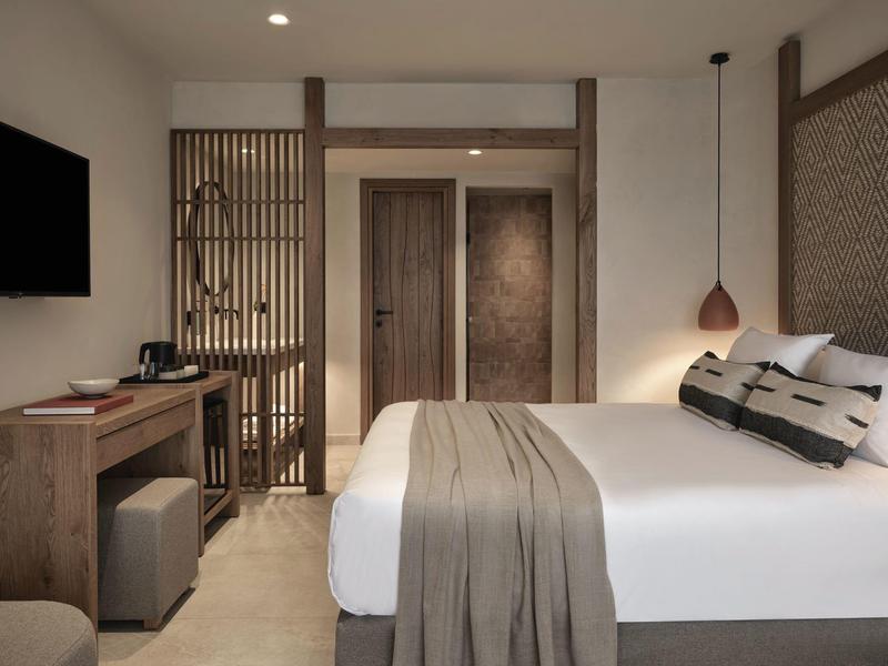 Chambre d'hôtel moderne avec grand lit, meubles en bois et lumière chaude.