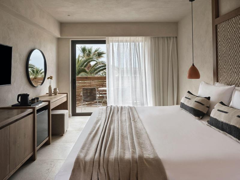 Chambre d'hôtel moderne avec grand lit, bureau, balcon et vue sur les palmiers.