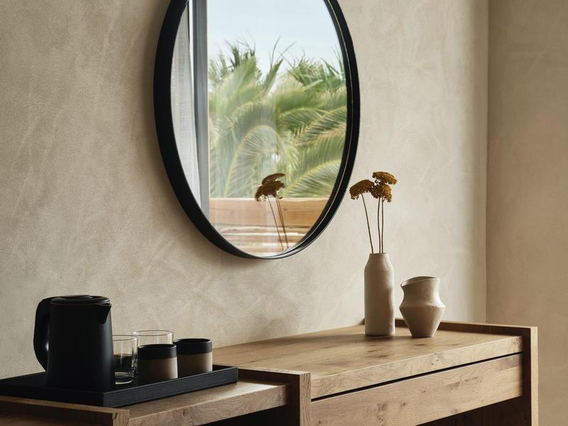 Table en bois moderne avec miroir rond et vases devant un mur couleur sable