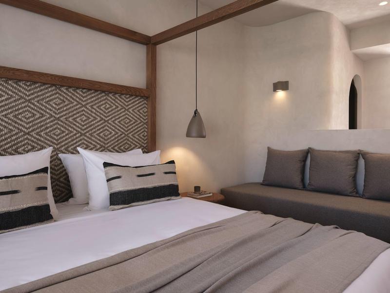 Chambre d'hôtel moderne avec lit double, canapé et décor minimaliste aux couleurs neutres.