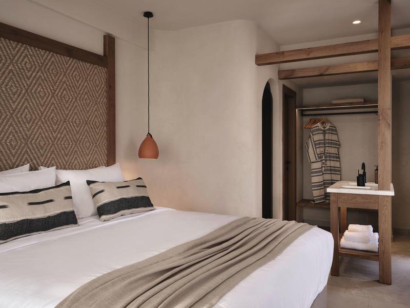 Chambre d'hôtel moderne avec grand lit, tête de lit décorative, mobilier en bois et éclairage chaleureux.