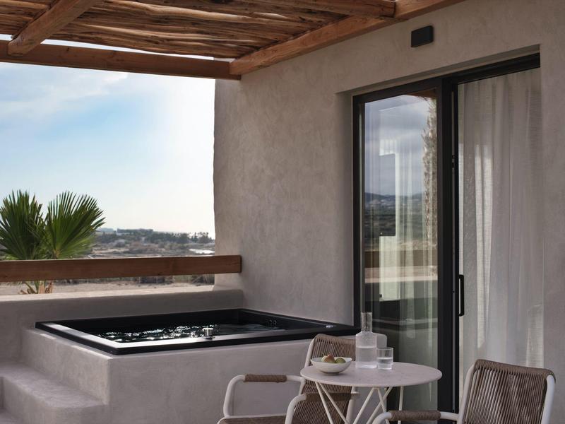 Balcon avec jacuzzi, petite table et chaise près de la porte vitrée, vue sur des palmiers et le paysage.