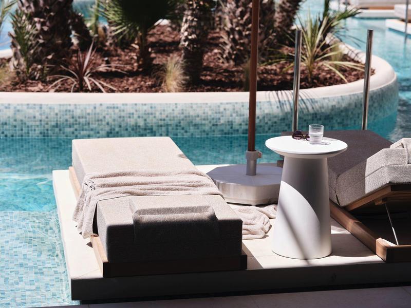 Vue de deux chaises longues avec des serviettes près d'une piscine et des palmiers en arrière-plan.