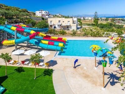 Bunter Wasserrutschenpark mit Schwimmbecken, Sonnenschirmen und grüner Liegewiese bei klarem Himmel.