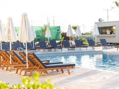 Leere Liegestühle und Sonnenschirme neben einem Pool in einer Hotelanlage bei Sonnenschein.