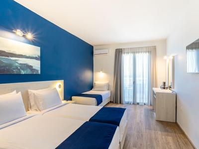 Modern eingerichtetes Hotelzimmer mit Doppel- und Einzelbett, blauer Akzentwand und Balkon