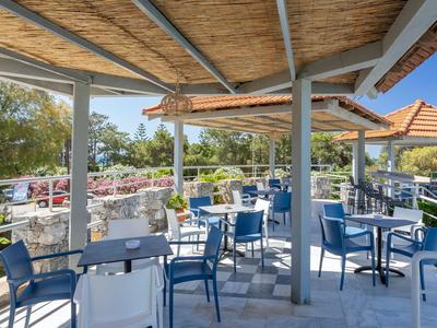 Überdachte Terrasse mit blau-weißen Stühlen und Tischen, umgeben von Natur und Sonnenschirmen.