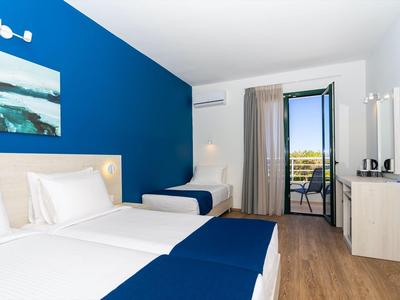 Hell eingerichtetes Hotelzimmer mit blauer Akzentwand, zwei Betten und Balkon mit Aussicht.