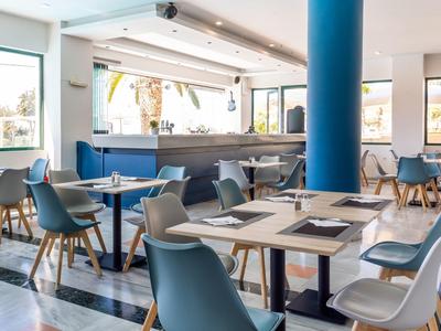 Modernes Café mit blauen Sesseln, Holztischen und großen Fenstern für viel Tageslicht.