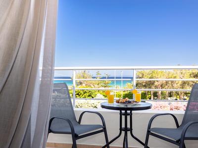 Balkon mit zwei Stühlen, Tisch mit Getränken, Blick aufs Meer und blauer Himmel im Hintergrund.