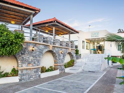 Moderner Hotelkomplex mit Steinmauer, Treppen und einer Terrasse unter klarem Himmel