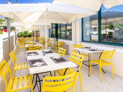Terrasse eines Restaurants mit gelben Stühlen und weißen Tischen unter großen Sonnenschirmen.
