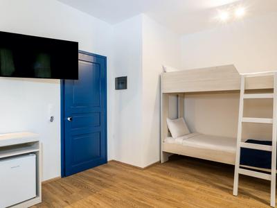 Kleines, schlichtes Zimmer mit Etagenbett, blauer Tür, Fernseher und Mini-Kühlschrank.