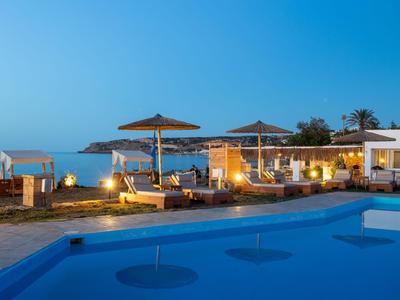 Luxuriöser Poolbereich mit Liegestühlen und Sonnenschirmen am Meer bei Sonnenuntergang.