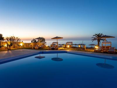 Abendliche Poollandschaft mit Sonnenliegen und Schirmen am Meer.