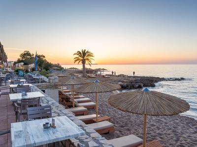 Strandpromenade mit Tischen, Stühlen, Sonnenschirmen und Palmen bei Sonnenuntergang am Meer.