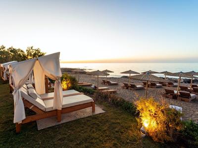 Strand mit Liegen, Sonnenschirmen und einer überdachten Holzliege vor Sonnenuntergang.