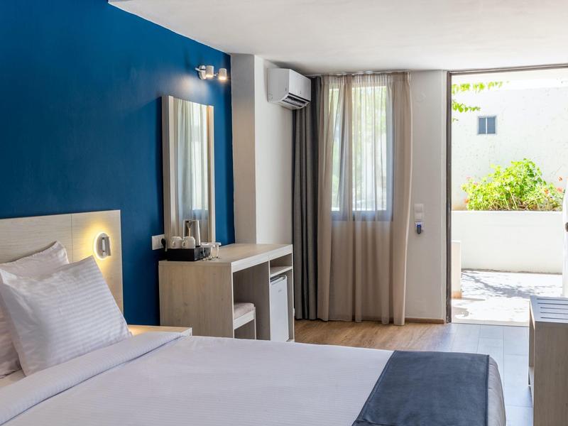 Heller Hotelraum mit blauem Akzentwand, Doppelbett, Schreibtisch und Fenster zur Terrasse.