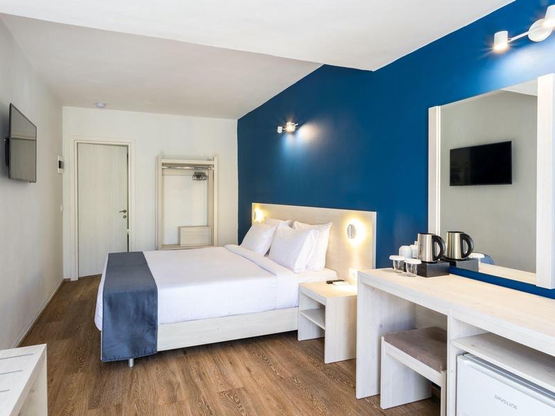 Modernes Hotelzimmer mit blau-weißer Wand, Doppelbett, TV, Schreibtisch und Holzboden.