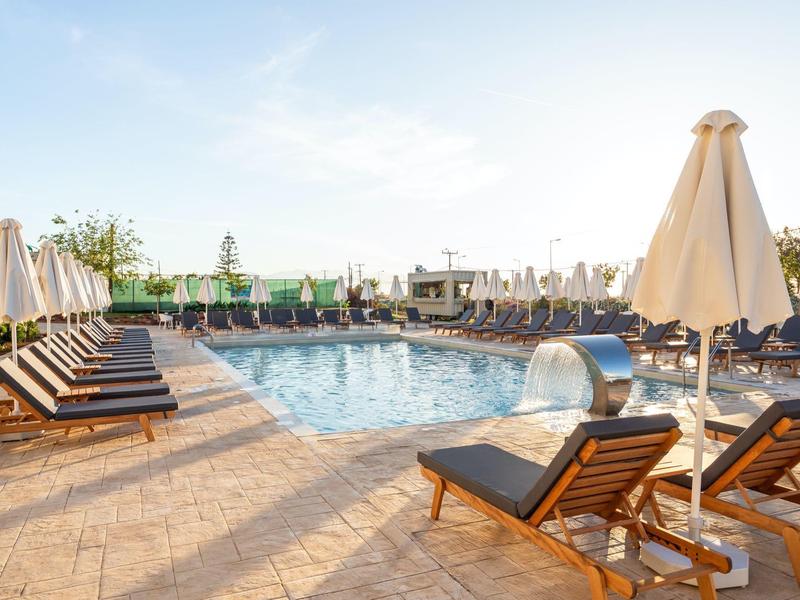 Freier Pool mit braunen Liegestühlen und geschlossenen beigen Sonnenschirmen bei Sonnenschein.