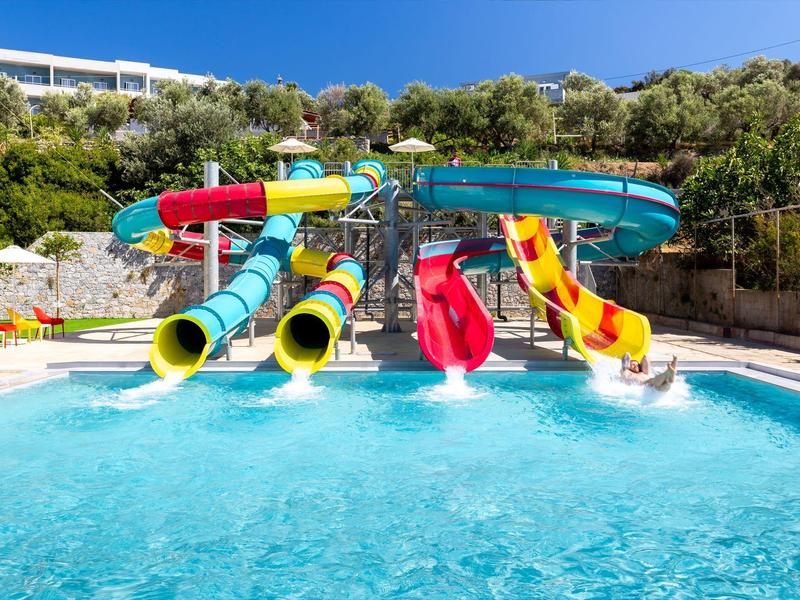 Bunte Wasserrutschen führen in ein klares Schwimmbecken mit blauem Himmel und grünen Bäumen.
