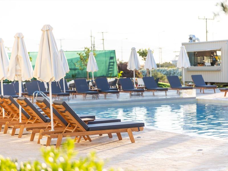 Schwimmbad mit blauen Liegestühlen, weißen Sonnenschirmen und Becken unter hellem Tageslicht.