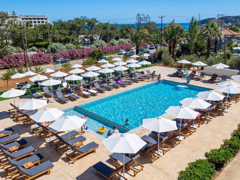 Großer rechteckiger Pool mit weißen Sonnenschirmen und Liegen, umgeben von grünen Pflanzen.