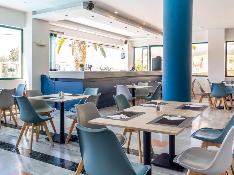 Modernes Café mit blauen Sesseln, Holztischen und großen Fenstern für viel Tageslicht.