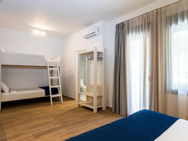 Helles Zimmer mit Etagenbett, Holzfußboden, Spiegel und Fenster mit Vorhängen.