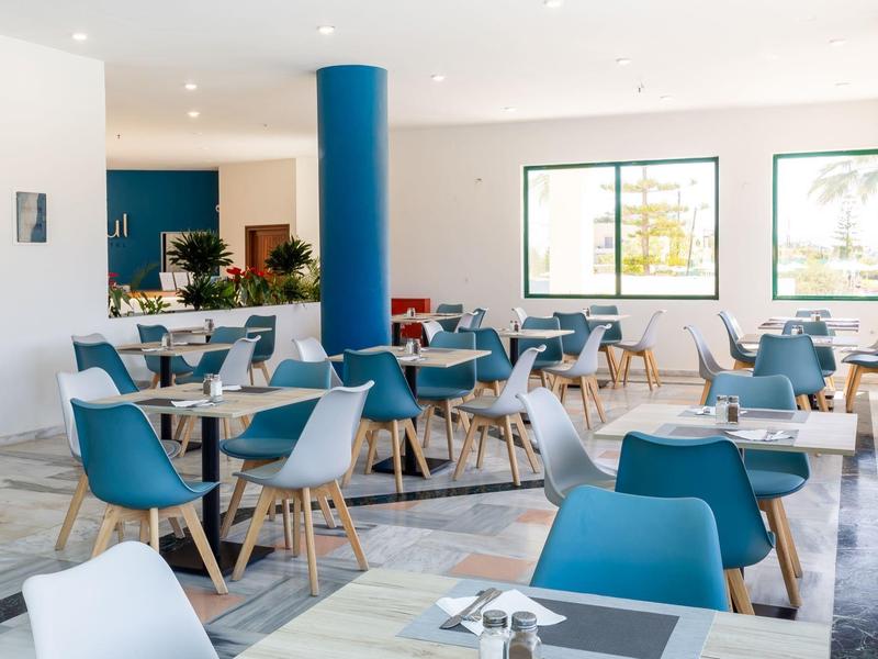 Helles, modernes Café mit blauen Sesseln, Holztischen und großen Fenstern für Tageslicht.