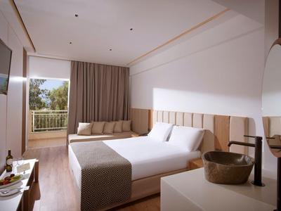 Habitación de hotel moderna con cama grande, balcón y decoración sencilla en tonos neutros.