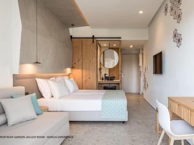 Camera d'hotel moderna con letto matrimoniale, divano, scrivania e bagno aperto sullo sfondo.