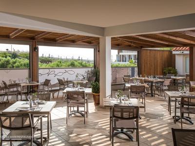 Area ristorante aperta dell'hotel con tavoli apparecchiati e vista sul verde.